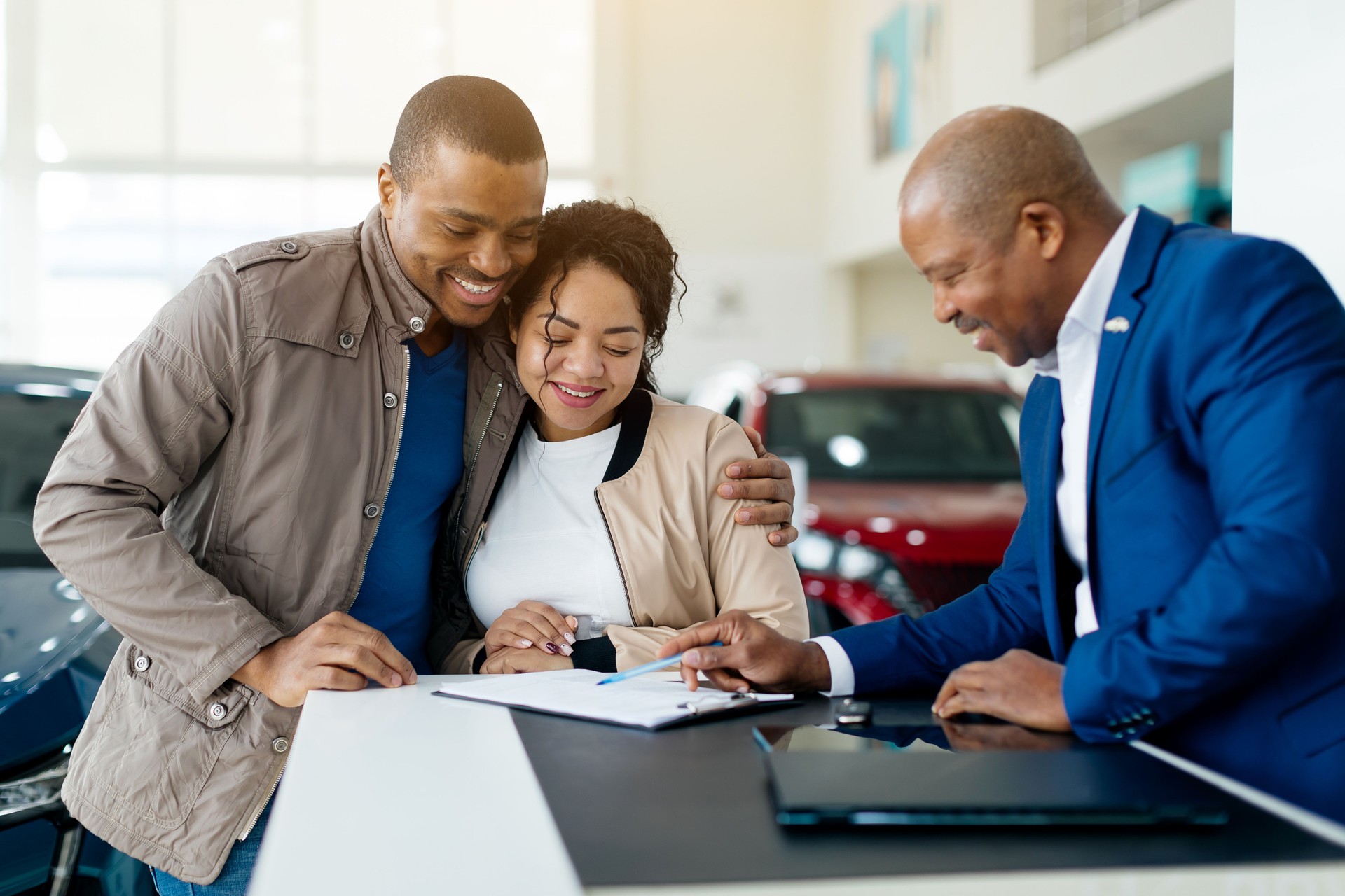 African American Couple signs purchase agreement at car dealership with attentive salesman assisting in car buying process